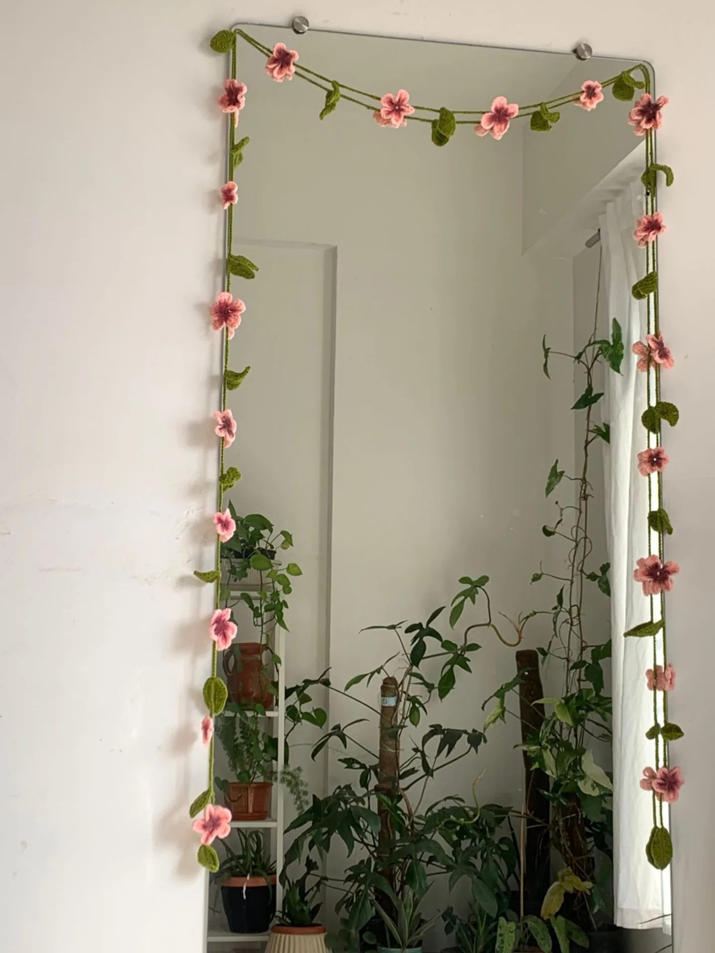 Pink crochet flower vine framing a mirror, surrounded by houseplants.